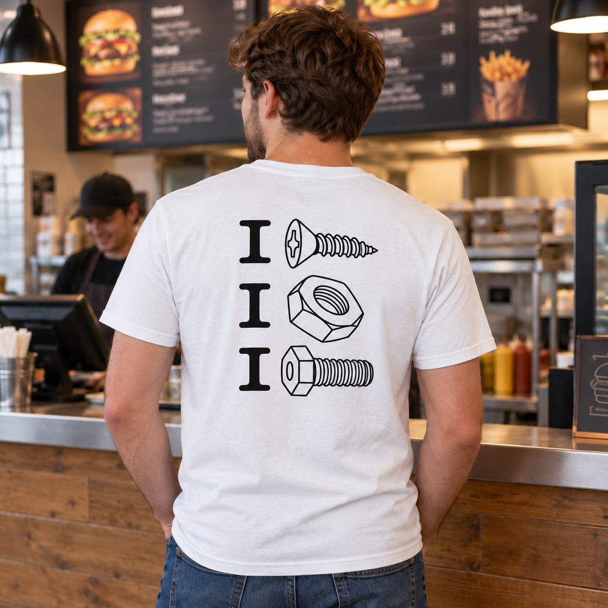 Lifestyle mockup of a man wearing the white screw nut bolt back-print T-shirt at a burger takeaway counter.